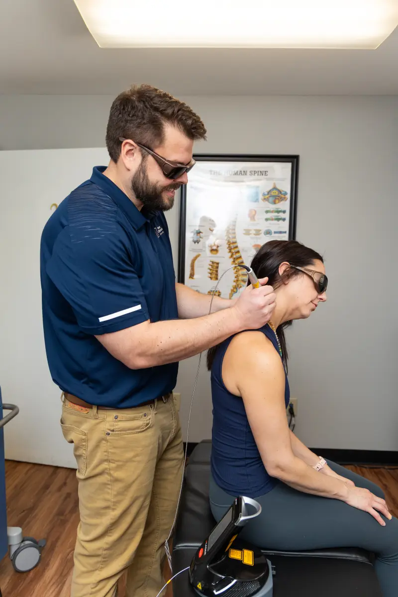Dr. Kyle Pelphrey treating a patient's neck with a Class IV laser handpiece while the patient wears protective glasses, at Pelphrey Chiropractic in Lexington, KY